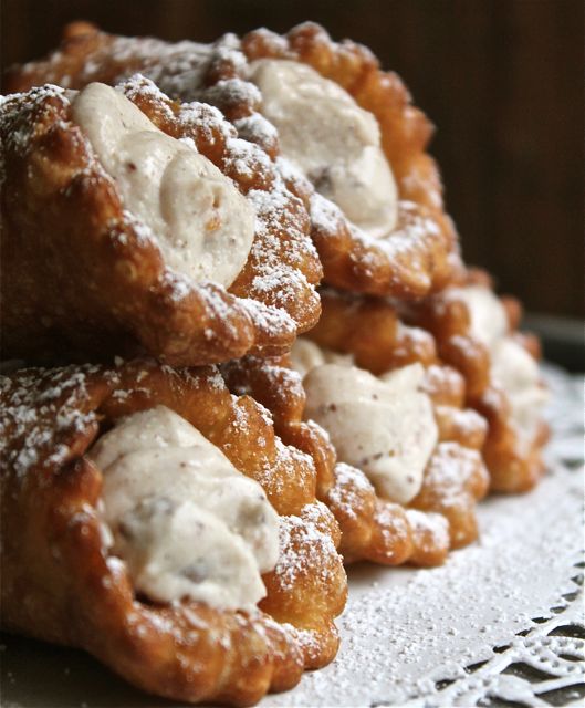 A close-up of Kannoli made in Malta, showcasing the crispy golden pastry shells filled with creamy ricotta cheese, adorned with colorful candied fruit, and dusted with powdered sugar. The Kannoli are artfully arranged on a plate, highlighting their exquisite presentation and inviting texture.