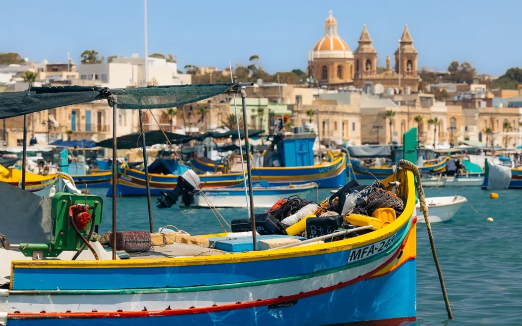 Colorful luzzu boats bobbing in the waters of Marsaxlokk, Malta. Their vibrant hues and iconic painted eyes create a picturesque scene against the blue sky and sea.