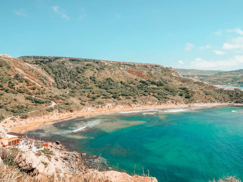 Għajn Tuffieħa, Malta: A serene beach with golden sands and clear blue waters, nestled between rugged cliffs and bathed in sunlight.