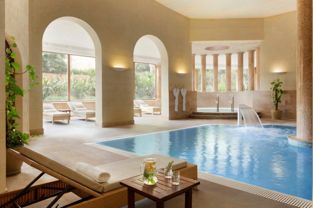 Interior of Kempinski Hotel San Lawrenz Spa, featuring serene ambiance, soft lighting, and modern wellness amenities. Guests relax in plush robes by the poolside or indulge in spa treatments amid elegant decor and tranquil surroundings.