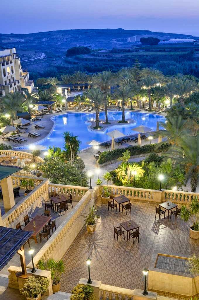 The outdoor pool area at Kempinski Hotel San Lawrenz, Gozo, Malta. The sparkling pool is surrounded by lush greenery and elegant lounge chairs, creating a serene oasis for relaxation and enjoyment. Guests can bask in the Mediterranean sun, take refreshing dips in the pool, or unwind with a drink from the poolside bar.