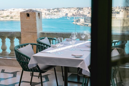 Outdoor seating area at ION Harbour restaurant, offering a captivating view of the picturesque Grand Harbour in Malta. The al fresco dining space is adorned with comfortable seating arrangements, stylish decor, and ambient lighting, creating an inviting atmosphere for guests to enjoy exquisite cuisine amidst the scenic backdrop of the harbor.