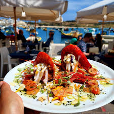 Liska Restaurant, located in Marsaxlokk, Malta, offers a charming waterfront dining experience. The restaurant's exterior features a vibrant facade with wooden shutters and colorful accents, reflecting the coastal charm of the fishing village. Diners enjoy al fresco seating overlooking the harbor, where traditional luzzu boats bob gently in the water. Inside, the restaurant boasts a cozy interior adorned with nautical decor, creating a welcoming atmosphere for guests to indulge in delicious Mediterranean seafood dishes.