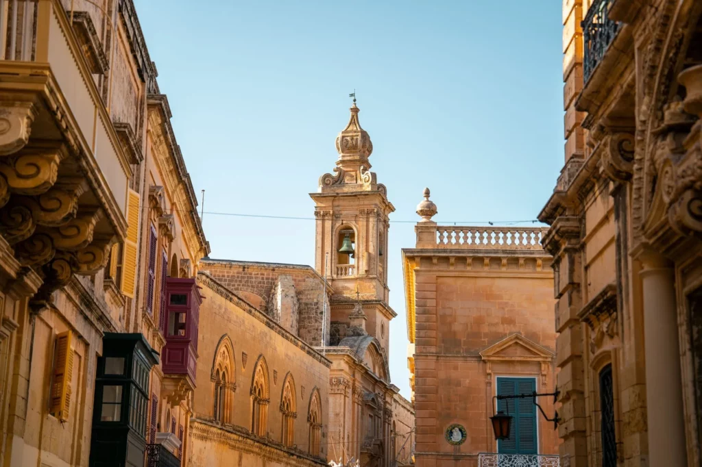 Aerial view of Mdina, Malta, showcasing its historic architecture, narrow winding streets, and imposing city walls, with sunlight casting shadows and highlighting the intricate details of the buildings.Aerial view of Mdina, Malta, showcasing its historic architecture, narrow winding streets, and imposing city walls, with sunlight casting shadows and highlighting the intricate details of the buildings.