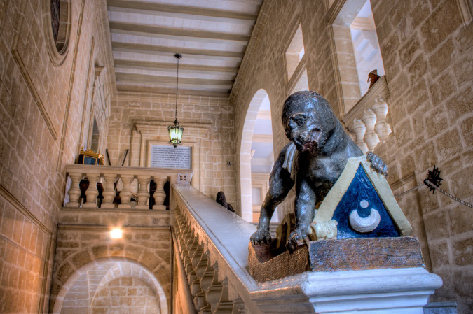 A panoramic view of the interior of a museum nestled within the ancient walls of Mdina, Malta. Visitors wander among the exhibits, which include ancient artifacts, historical relics, and artistic masterpieces. Soft lighting highlights the intricate details of each display, inviting exploration and discovery. The museum's ambiance exudes a sense of reverence and curiosity, offering a glimpse into Malta's rich cultural heritage and storied past.