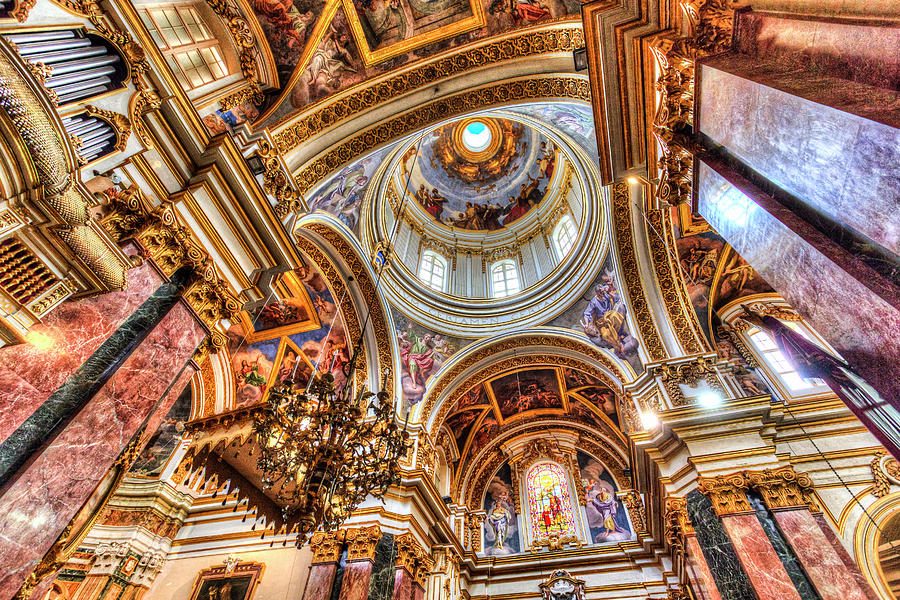 The majestic interior of the Co-Cathedral of St. Paul in Mdina, Malta, adorned with intricate Baroque architecture, gilded sculptures, and ornate frescoes. Sunlight streams through stained glass windows, casting vibrant hues upon the marble floors and intricately carved wooden pews. Visitors marvel at the cathedral's grandeur and spiritual significance, immersing themselves in the timeless beauty of this historic place of worship.