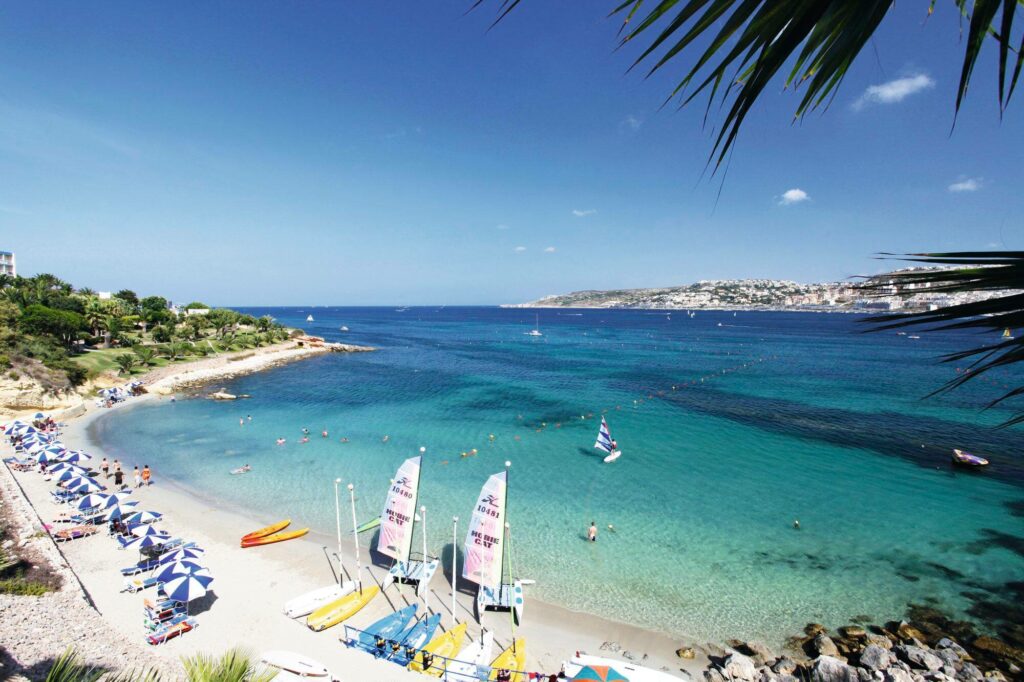 Mellieħa Bay: A panoramic view of the expansive sandy beach bordered by turquoise waters and backed by lush greenery.