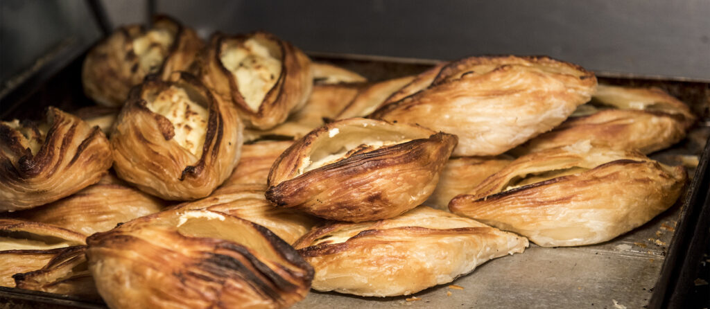 Close-up of freshly baked ricotta-filled pastizzi, a traditional Maltese snack, displaying flaky golden pastry and creamy ricotta filling.