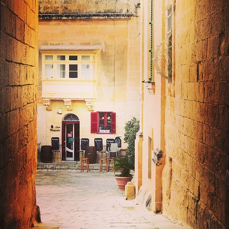 Don Mesquita, a renowned restaurant housed within a historic building in Mdina, Malta, exudes a timeless charm with its stone facade and traditional Maltese architecture. The exterior features arched doorways, wrought-iron lanterns, and wooden shutters, evoking a sense of old-world elegance. A sign above the entrance proudly displays the restaurant's name, while a vibrant array of flowers adorns the windowsills, adding a pop of color to the picturesque scene. Passersby are drawn to the inviting ambiance, eager to step inside and savor the authentic flavors of Maltese cuisine.