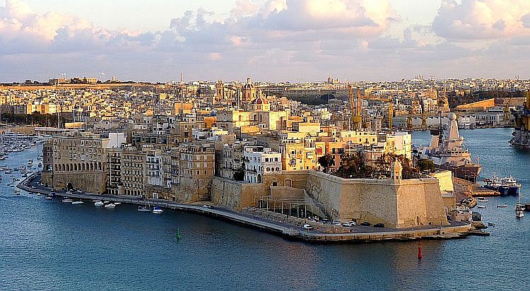 The quaint waterfront of Isla, Malta, bustling with activity. Colorful fishing boats and yachts line the marina, while historic buildings and fortifications overlook the scene. The shimmering waters of the Grand Harbour reflect the vibrant hues of the boats and the clear blue sky above. This picturesque view captures the essence of Isla's maritime charm and rich cultural heritage.





