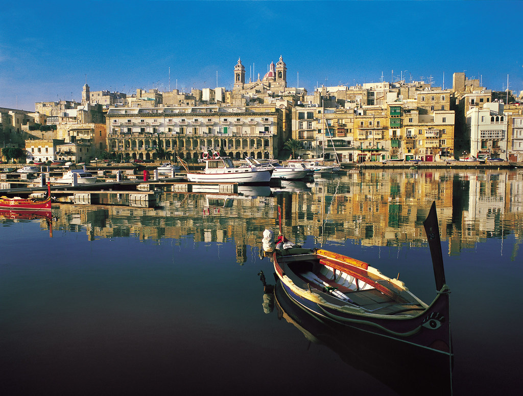 
Alt Image Description:
A traditional Maltese boat, known as a "dghajsa" or "luzzu," stationed at the waterfront of Isla. The vibrant colors of the boat's hull contrast beautifully with the azure waters of the Mediterranean Sea. In the background, historic buildings line the waterfront, creating a picturesque scene that captures the essence of Isla's maritime heritage.