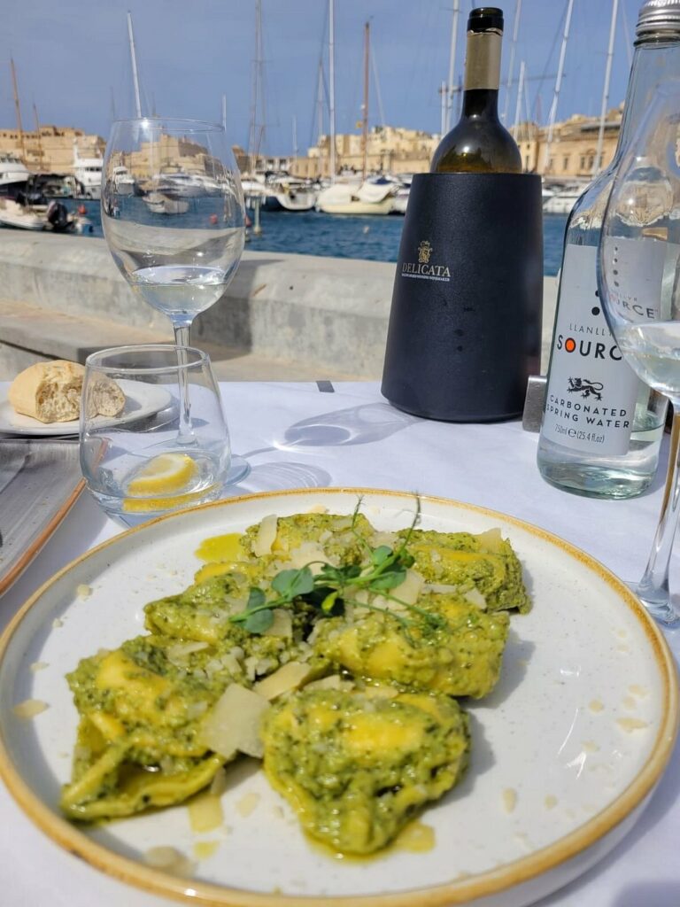 A mouthwatering plate of ravjul (Maltese ravioli) served at Il Hnejja restaurant in Senglea, Malta. The pasta parcels are generously filled with a savory mixture of ricotta cheese and spinach, topped with a rich tomato-based sauce and grated Parmesan cheese. Fresh basil leaves garnish the dish, adding a pop of color and aroma. The perfect balance of flavors and textures makes this traditional Maltese dish a delightful culinary experience.