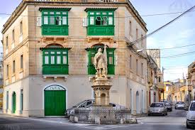 A picturesque view of the town of Qormi, Malta, revealing its charming streets lined with colorful buildings and traditional Maltese architecture. The town square bustles with activity as locals go about their daily routines, while historic landmarks and quaint shops dot the landscape, evoking a sense of timeless beauty and community.