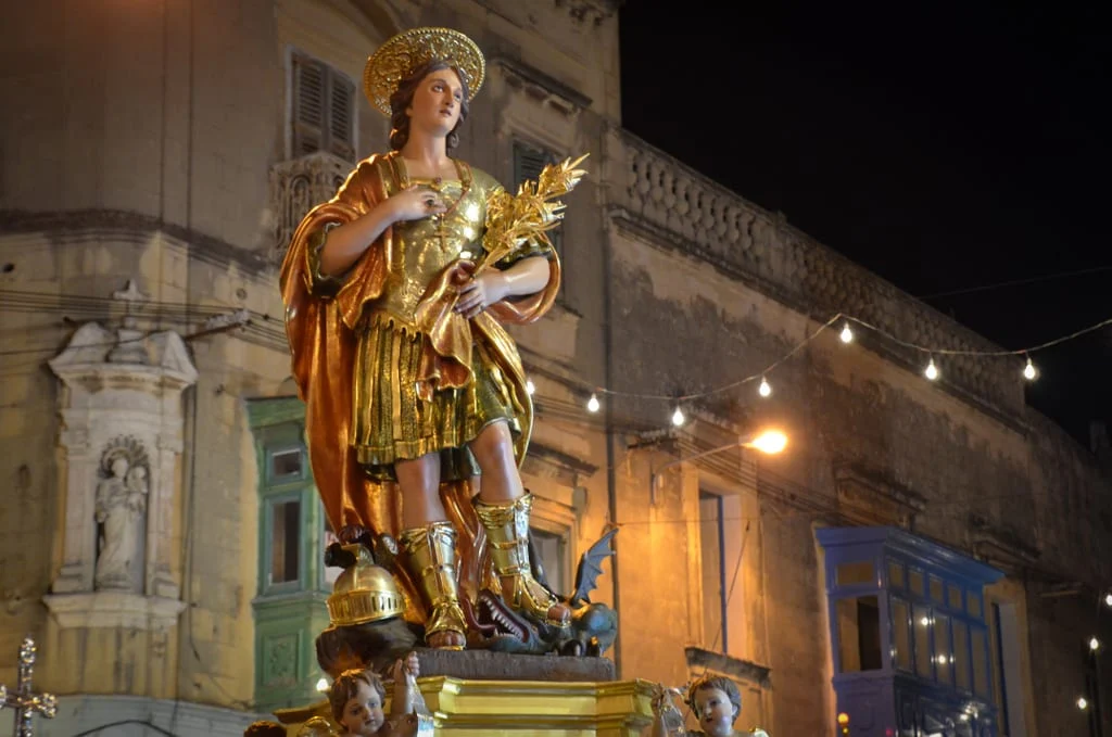 In the midst of jubilant celebrations in Qormi, Malta, the statue of St. George takes center stage, adorned with vibrant decorations and surrounded by enthusiastic crowds. The statue, a symbol of faith and tradition, stands tall amidst a sea of revelers, evoking a sense of reverence and joy. Colorful banners flutter in the breeze, while the sound of music and laughter fills the air, marking a festive occasion that honors the patron saint of Qormi in grand style.