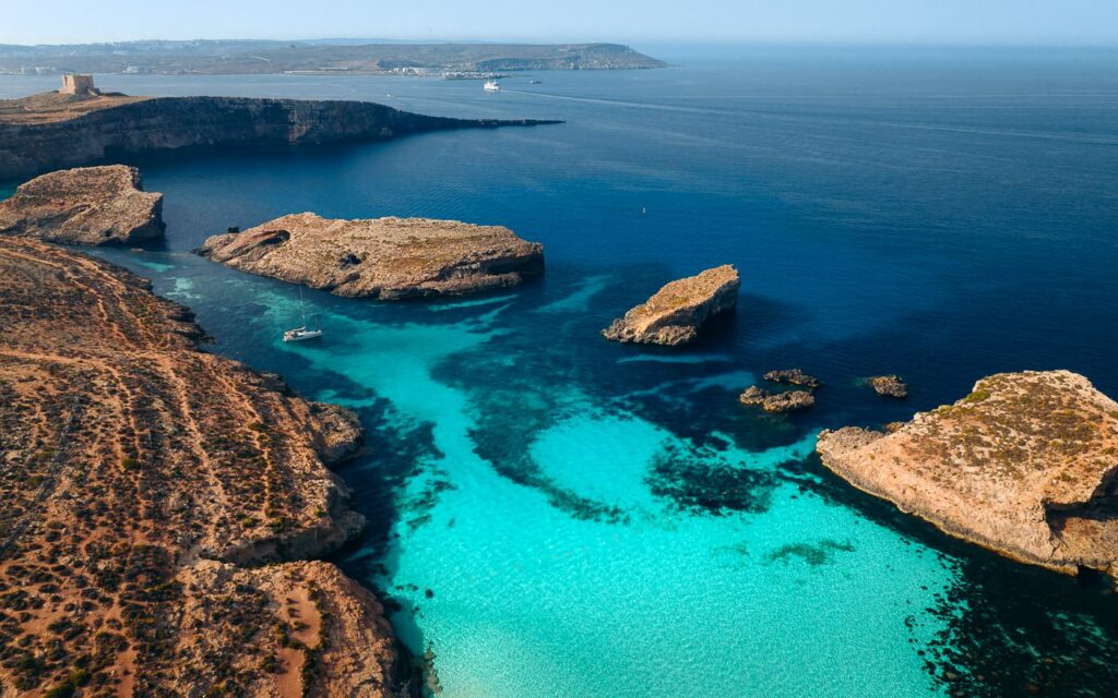 Tourists Enjoying Blue Lagoon: Tourists relaxing and swimming in the pristine waters of the Blue Lagoon on Comino Island, Malta, surrounded by the scenic rocky coastline.