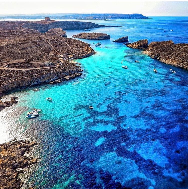 Blue Lagoon Beachfront: A picturesque beachfront of Comino's Blue Lagoon, with vibrant blue waters lapping against the sandy shore, framed by lush greenery and rocky cliffs.