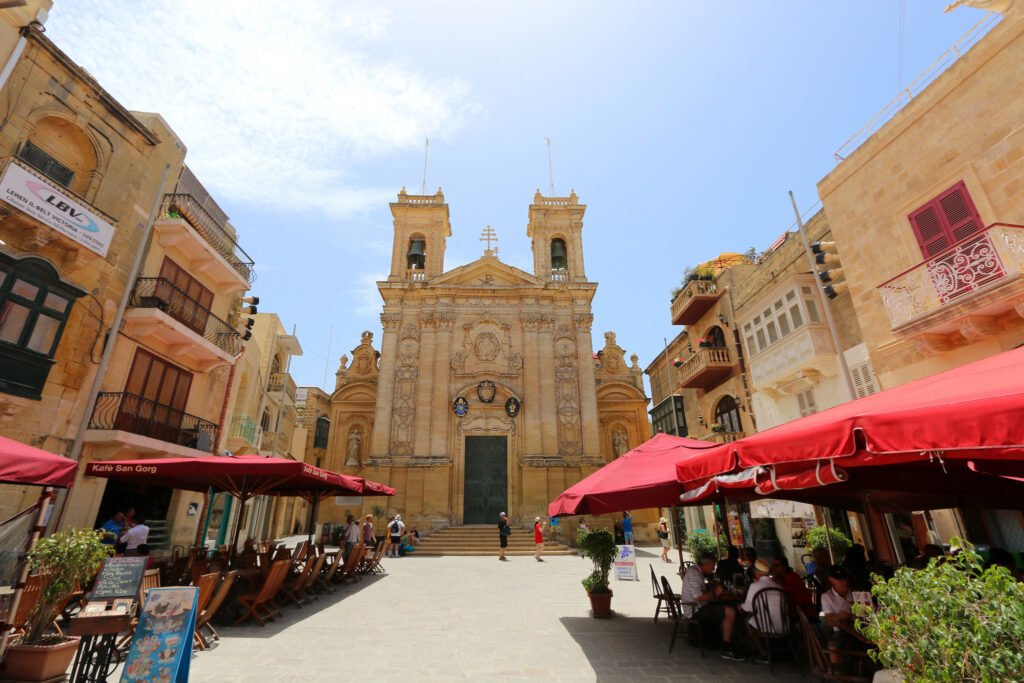 Local Gozo scene featuring picturesque countryside, traditional Maltese architecture, and a stunning view of the sea.