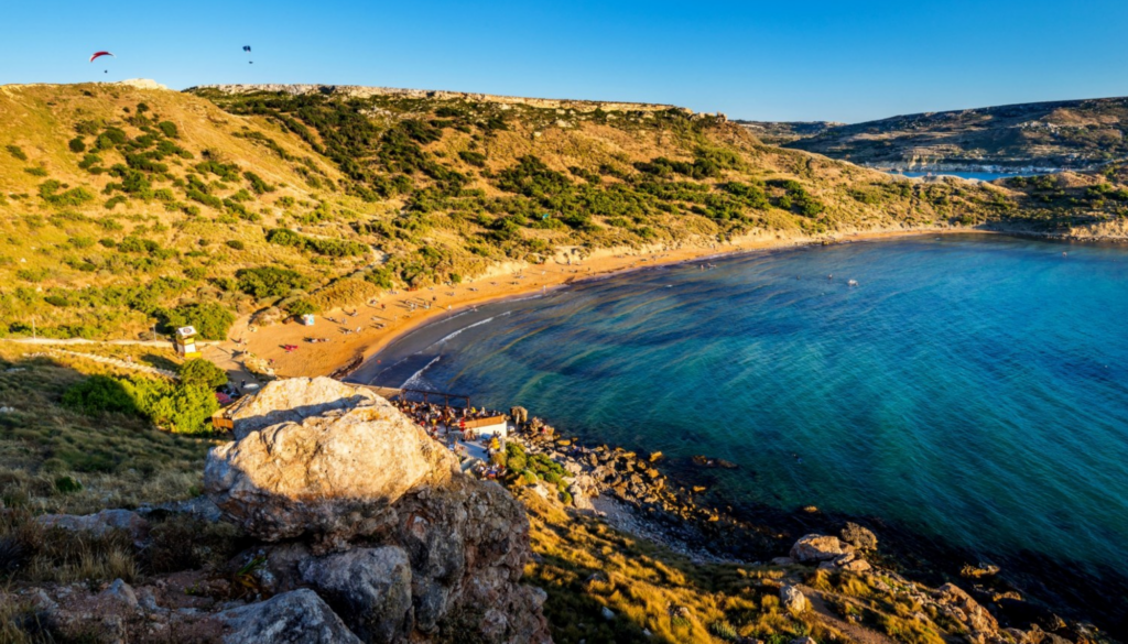 Beautiful Mediterranean beach in Malta at sunrise with golden-orange sand and a vibrant sky.